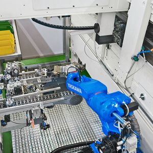 Der Motoman MH12 holt Rohteile am oberen Förderband ab und legt die bearbeiteten Fertigteile auf dem unteren Band wieder ab.				