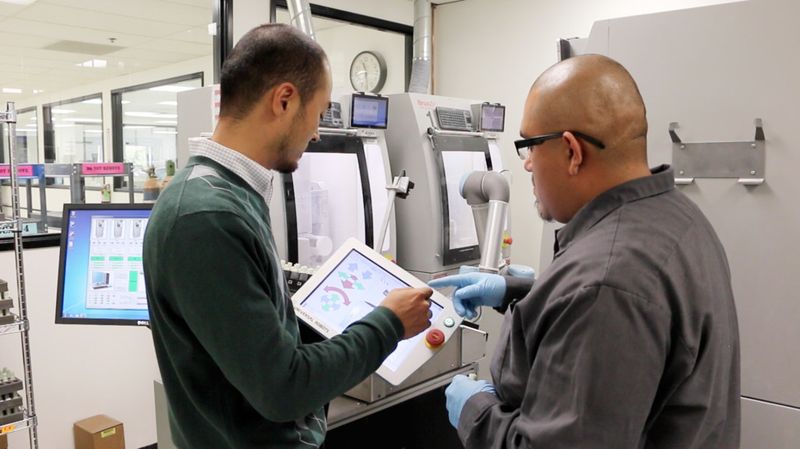 Der Automatisierungsingenieur Daniel Phee (li.) weist den Bediener der Fräsmaschine Jose Flores in den UR5-Roboter ein. (Bild: Universal Robots)