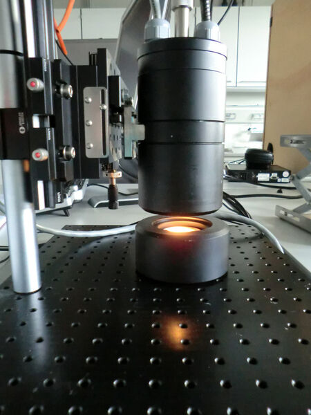 Aufbau für die NIR-spektroskopische Analyse von HTC Produkten in diffuser Reflexion. Der Messkopf ist mittels Glasfaser an das NIR-Spektrometer (nicht abgebildet) angeschlossen. Eine Messung benötigt weniger als 1 Sekunde. Unterschiedliche Sonden bzw. Messköpfe können an das Spektrometer angeschlossen werden und der Messaufbau so an unterschiedliche Messbedingungen angepasst werden. (Fh-ICT)