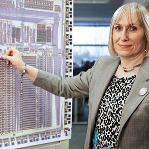 Sophie Mary Wilson hält 2013 vor ein vergrößertes Foto der ersten ARM-CPU ein Foto einer aktuellen ARM-Cortex-CPU im selben Maßstab.(Bild:  Sophie Wilson /Chris Monk / CC BY-SA )
