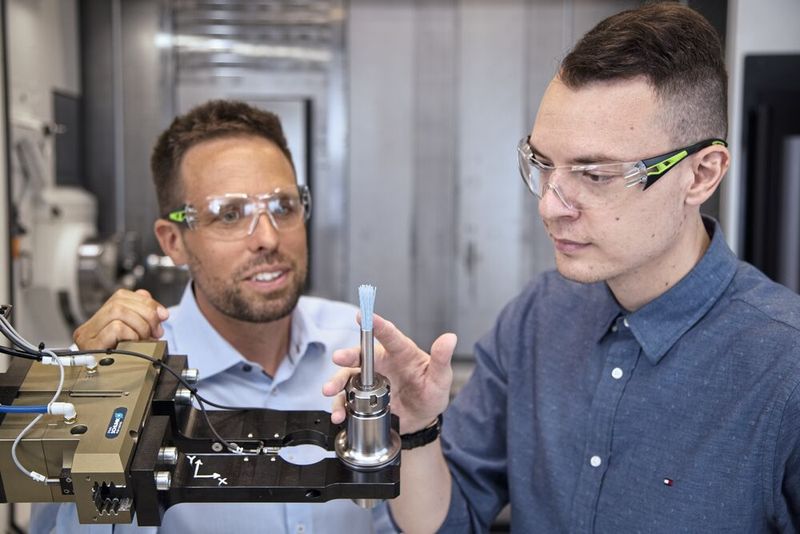 Dominik Rothenberger (li., Technischer Aussendienst, Zeintra AG) und Zarko Milic (Leiter Serienteilefertigung, Herzog Systems AG) begutachten eine Pinselbürste. Bei höheren Drehzahlen wird die Spreizung der Bürste genutzt, um in den Bohrungen der Bauteile die Grate zu entfernen. (Bild: Matthias Böhm)