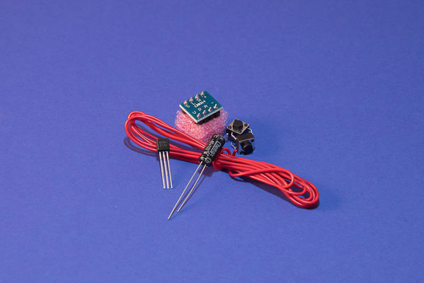 Bild 7: Die rote Leitung für die Antenne und die zu fertigenden unzählligen Drahtbrücken. Daneben zu sehen Leistungstransistor, Elko, Taster und Empfänger-Schaltkreis BK1068. (Bild: Kristin Rinortner)