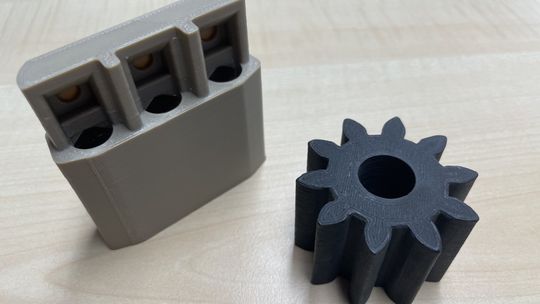 Zwei Werkstoffe, ein Anspruch: Hochvoltstecker aus unverstärktem PEEK und Zahnrad aus kohlenstofffaserverstärktem CF-PEEK, gefertigt im Filamentdruck. (Bild:  Malping GmbH)