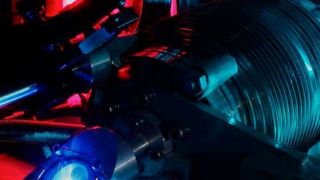 Dieses Foto zeigt den Vakuumapparat, der zur Messung der 2S-4P-Übergangsfrequenz in atomarem Wasserstoff genutzt wurde. Das violette Leuchten im Hintergrund stammt aus der Mikrowellenentladung, die Wasserstoff-Moleküle in Wasserstoff-Atome dissoziiert. Das blaue Licht im Vordergrund ist Fluoreszenz vom ultravioletten Laser, der die Atome in den 2S-Zustand anregt. Das türkisfarbene Leuchten ist Streulicht von dem Lasersystem, das zur Frequenzmessung des 2S-4P-Übergangs dient.  (MPQ)