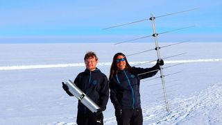DESY-Physiker Christoph Welling (l.) und DESY-Physikerin Ilse Plaisier mit einer der Radioantennen des neuen Neutrino-Detektors auf Grönland.  (Bild: RNO-G, Cosmin Deaconu)