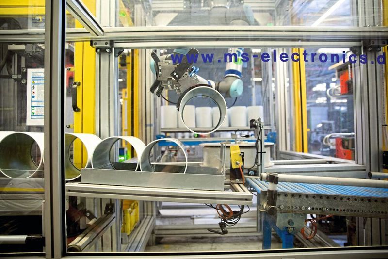 Der UR10e ist zwischen zwei Klinkstationen fest installiert. Dort werden Löcher in Blechzylinder eingestanzt, die später zu Tretmülleimern weiterverarbeitet werden. (Universal Robots)