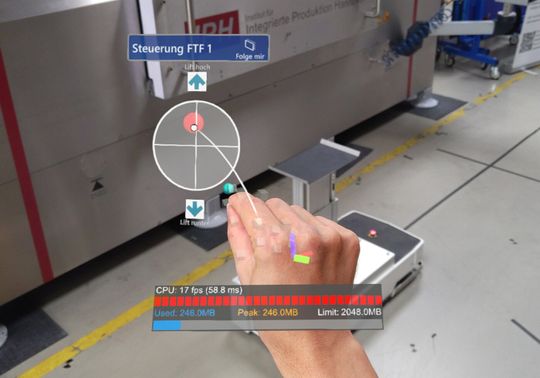 (Blick durch die AR-Brille: Der Screenshot zeigt die Benutzeroberfläche für die Gestensteuerung. Logistikmitarbeiter müssen lediglich den roten Punkt greifen, der als virtueller Joystick dient – schon können sie das Fahrzeug bewegen. Foto: IPH, Florian Kreutzjans)