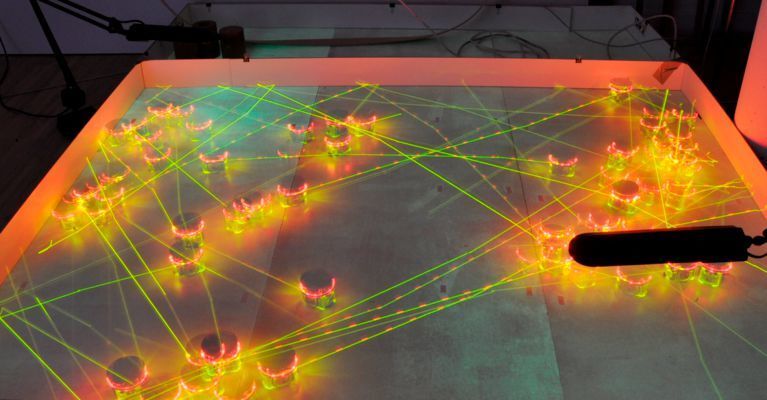 Langzeitbelichtung eines ePuck-Roboter-Schwarms, der den BEECLUST-Algorithmus ausführt. Es sind deutlich einige Cluster zu sehen, zwischen denen Roboter ausgetauscht werden (gerade Linien) (Artificial Life Lab, Universität Graz)