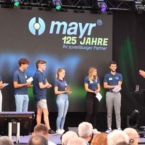 Fachkräfte sind ein rares Gut und ein wichtiger Erfolgsfaktor. Das weiß auch Ferdinand Mayr, CEO und Geschäftsführender Gesellschafter von Mayr Antriebstechnik. Hier auf der Bühne mit sechs von insgesamt ach Auszubildenden, die stellvertretend ihre Wünsche für die Zukunft des Unternehmens vorbrachten. (Bild:  Mayr Antriebstechnik)