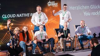 Daniela Schilling, Leiterin der Vogel IT-Akademie, auf der Bühne mit den sitzenden CLOUD NATIVE ROCKSTARS, Emma Wehrwein (eco – Verband der Internetwirtschaft), Sebastian Langer (in Vertretung für Michael Schöller, Schmitz Cargobull), Stefan Pfaffel (Allianz Technology) und Benny Woletz (Cloudwürdig), mit ihnen freuen sich Fabian Früchtenicht (Schmitz Cargobull / NeoGeo New Media GmbH) und Alex Pöllmann (Viessmann, oben, v.l). (Bild: berndrottmann.com)