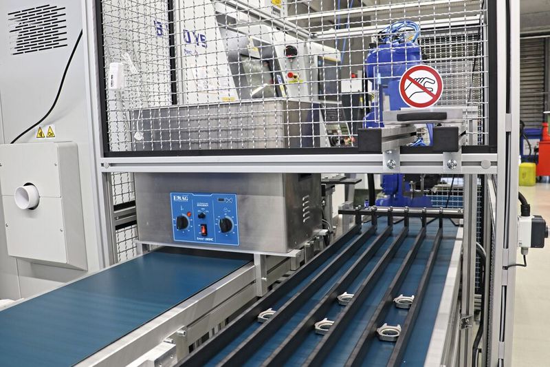 Automatisierungszelle für die Bearbeitung geschmiedeter Uhrgehäuse: Auf dem rechten Förderband fahren die Rohlinge in die Roboterzelle und links kommen die Fertigteile heraus. (Bild: teamtec)