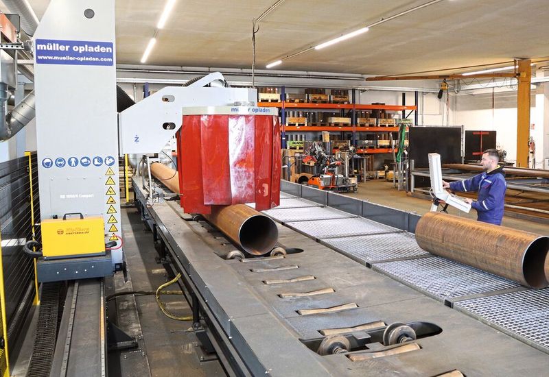 Über einen 16 Meter langen Rollgang-Förderer werden die außerhalb der Halle gelagerten Rohre bis 8.000 Kilo Stückgewicht der Schneidanlage zugeführt. Der vollautomatisierte Schneidtisch der Anlage besitzt 12 höhenverstellbare Rohrunterstützungen, die sich automatisch der zum Teil unrunden Rohroberfläche anpassen und so für eine perfekte Auflage über die gesamte Rohrlänge sorgen. (Bild: Müller Opladen)