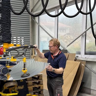 Mit dem Vakuum-Schlauchheber „heavyLIFT“ von Timmer entnimmt ein Mitarbeiter von Lo-Cat Systems das gewölbte Aluminiumblech präzise und schonend aus der Rundwalze. (Bild: Lo-Cat Systems)