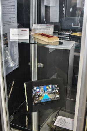 Viitrine von Meilensteine-Awardträger Sharp (Kategorie Displays): Zu sehen sind der Ever Sharp Pencil von 1915, der weltweit erste LCD-Taschenrechner von 1973 sowie ein aktuelles Free-Form-Display für den Automotive-Einsatz. (Fotostudio SX Heuser)