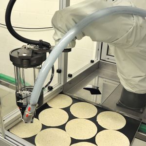 Roboter beim Dressieren von Tortenböden. Wie alle Konditoren in der Backstube trägt auch er einen weißen Schutzanzug. Nur die Haube bleibt ihm erspart.