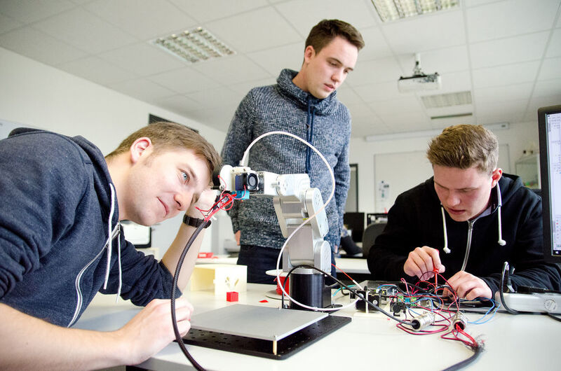 Aaron Müller, Marius Artmann und Michael Koschny (v.l.) tüfteln noch am Gehäuse ihres 3D-Druckers, den sie in einen sechsachsigen Roboter integriert haben. (FH Münster)