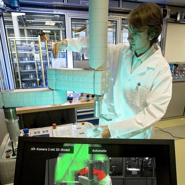 Optische Arbeitsraumüberwachung für einen Roboter am Fraunhofer IFF. Auf dem unteren Bildschirm ist ein sonst nicht sichtbarer Lichtkäfig eingeblendet. Der Roboter unterbricht seine Bewegung, sobald ein Mensch in den Arbeitsraum eindringt. (Bild: Uwe Völkner Fraunhofer IFF)