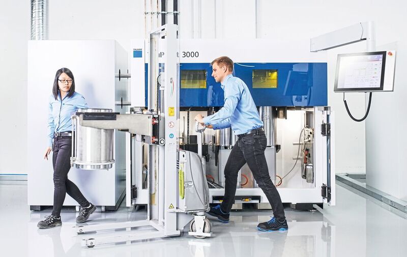 Additive Manufacturing: Mitarbeiter holen den Zylinder mit dem Bauteil
aus dem 3D-Drucker zur Weiterverarbeitung. (TRUMPF GmbH + Co. KG)