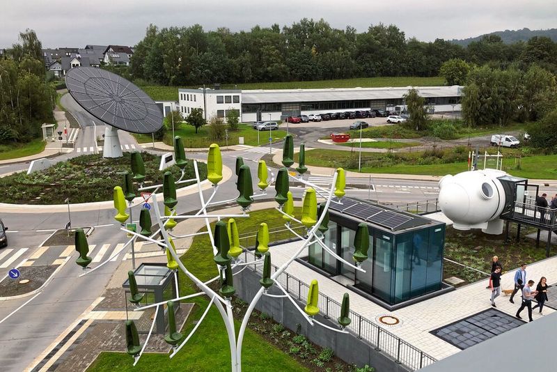 Der All Electric Society Park in Blomberg: Hinten links befindet sich im Kreisel das Erkennungszeichen, ein Solartracker mit einem Durchmesser von 12 Metern. Er lässt sich um die Zentralachse zur Sonne drehen, vorne im Bild steht ein Windenergieerzeuger in Baumform, rechts sieht man einen Cube und eine begehbare Windgondel. (Bild:  VCG/A. Unger-Leinhos)