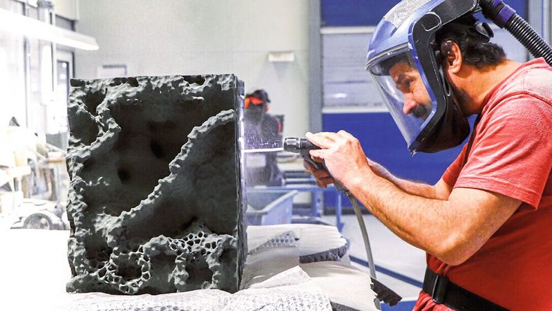 Nachbearbeitung eines Teilstücks der additiv gefertigten Meristem Wall: ein Mitarbeiter entfernt den unverdruckten Sand mittels Druckluft vom Bauteil.(Bild:  voxeljetAG)