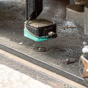 Ein RFID-Sensor von Pepperl+Fuchs sorgt für die genaue Positionierung des Zuges über den Movitrans-Ladeplatten. Für die Bahnhofanfahrt werden fünf RFID-Tags (kleine schwarzen Scheiben im Bild) benötigt. Mit diesem Sensor können verschiedene Signale entlang der Fahrstrecke empfangen oder beispielsweise auch der Zug in bestimmten Abschnitten in seiner Geschwindigkeit begrenzt werden, etwa bei Bergabfahrt.(Bild:  SEW)