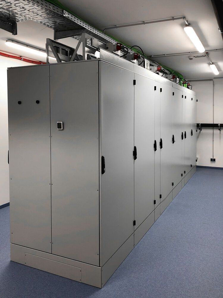 Rückseitige Ansicht der bei Kleusberg installierten „IS-1“-Racks mit oben liegender Kabeltrasse und Abgangskästen.