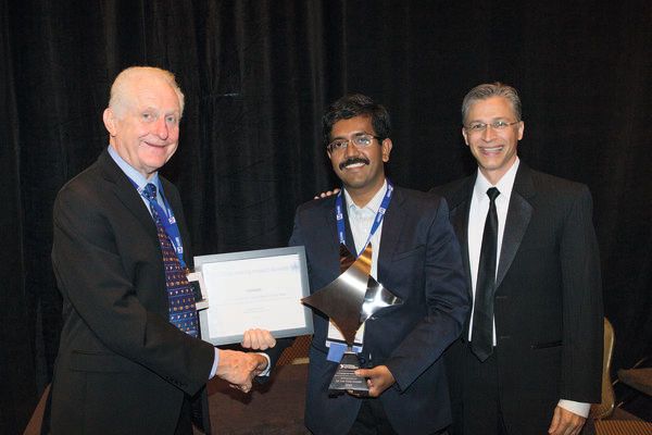 Auszeichnung: Dr. Joseph Jayaraj, Systemarchitekt am Healthcare Technology Innovation Centre (Mitte), empfängt den Engineering Impact Award aus den Händen von Dr. James Truchard, dem Mitbegründer und CEO von National Instruments. Rechts: Dave Wilson, Academic Marketing Director von NI. (National Instruments)