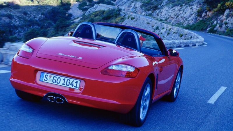 Anfang der 1990er-Jahre geriet Porsche in eine Absatz- und Ertragskrise. In diese Zeit und in den vom Mazda MX-5 gestarteten Roadster-Boom hinein fiel die Entscheidung über die Entwicklung eines Mittelmotor-Roadsters. Das Ergebnis dieser Entwicklungsarbeit war der Porsche Boxster, dessen Name ein Kunstwort aus den Worten Boxer(-Motor) und Roadster darstellt. Mit seiner Mittelmotorbauweise trat er gegen konventionelle Typen wie BMW Z4, Mercedes SLK oder Audi TT an. (Bild: Porsche)
