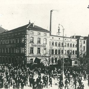 Historische Außenaufnahme (ca. 1920) der Fabrik von Reiniger, Gebbert & Schall (RGS) an der Luitpoldstraße in Erlangen. Das Gebäude wird 1893 bezogen und verfügt über zahlreiche Werkstätten und Büros. Im Vordergrund: Arbeiter verlassen nach Feierabend die Fabrik.