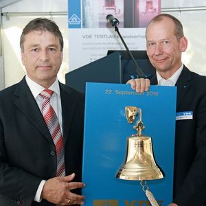 Mit den Worten „Möge sie nie zum Einsatz kommen“ überreichte Wolfgang Niedziella, Geschäftsführer des VDE-Instituts (links), dem Leiter des Brandprüfzentrums der VDE Prüf- und Zertifizierungsinstitut GmbH, Detlef Staemmer, anlässlich der Eröffnung des Testlabors eine Feuerglocke.