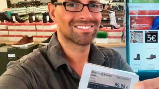 Georg Mahn von Schuhplus präsentiert stolz ein digitales Display, im Hintergrund ist ein Touch-Stahdisplay im Fachgeschäft zu erkennen.  (Schuhplus)