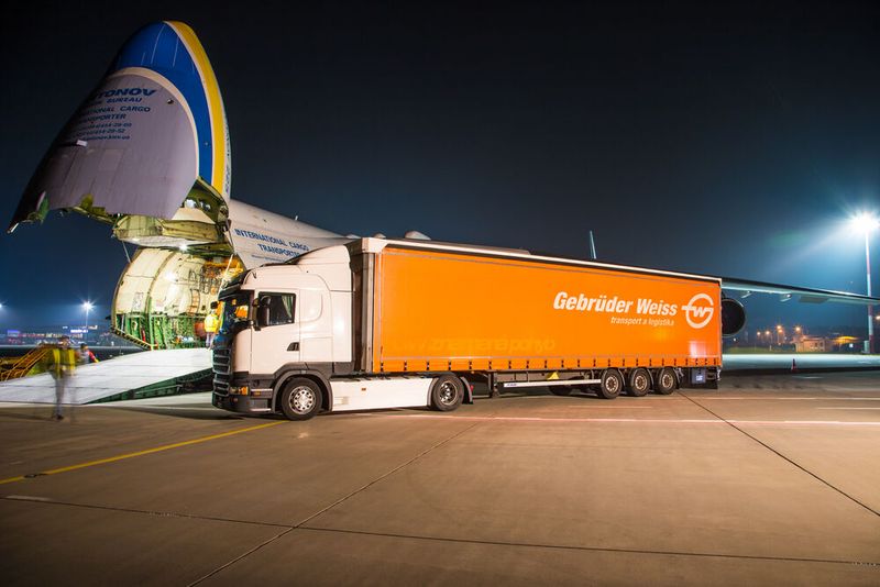 Ein Lkw von Gebrüder Weiss nähert sich dem aufgeklappten Bug der Antonov An-225, durch den die Versuchsladung für das Projekt ins Innere der Riesenmaschine gebracht werden kann. (Bild: Gebrüder Weiss / D. Szymula)