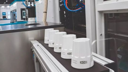 A joint project by Rea Elektronik and Dr. Boy at Fakuma 2026: The freshly moulded coffee mug is automatically fed into the laser cabin for custom marking.(Source:  Rea Elektronik)
