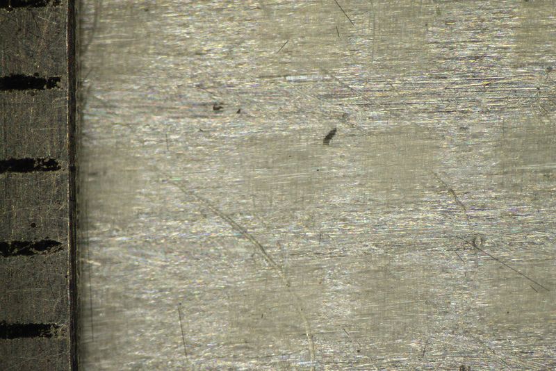 GFK-Aluminium-Hybridwerkstoff im Lichtmikroskop mit Millimeterskala vor (links) und (rechts) nach dem Versagen im Zugversuch – Faserrichtung von links nach rechts [1]. Nach dem Versagen der Fasern übernimmt auch hier die noch intakte Aluminiumlage die Last. (Beuth Hochschule)