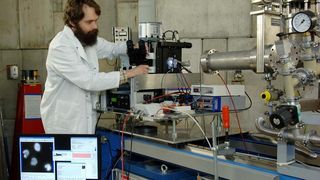 GSI-Wissenschaftler Burkhard Jakob am Messplatz zur Beobachtung der Reparaturvorgänge bei DNA-Schäden. Durch das waagerechte metallische Rohr von rechts kommt der Ionenstrahl und trifft auf die Zellprobe an der erleuchteten Stelle in der Mitte des Bildes.  (Bild: GSI)