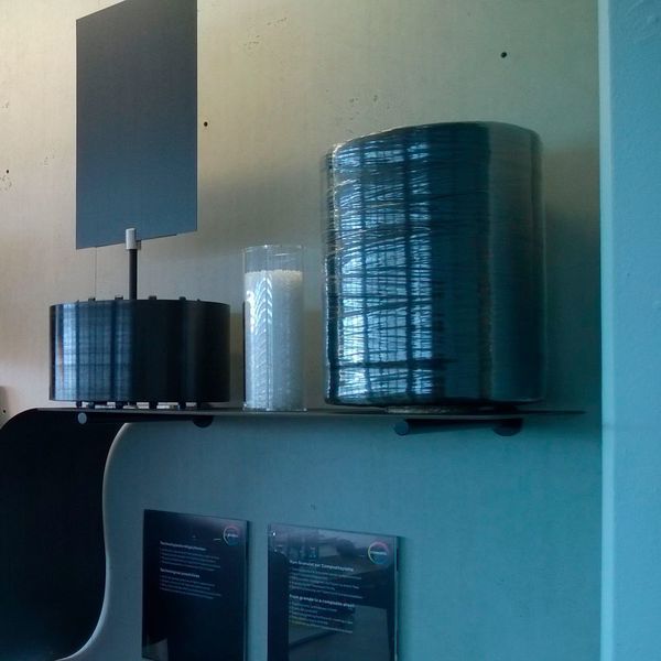 Bei der Produktion von CFRTPs werden z.B. Kohlenstoff-Fasern mit Polycarbonat getränkt und mit einer Breite von ca 800 mm auf Spulen gewickelt. Im zweiten Verfahrensschritt werden die Tapes auf Länge geschnitten und im 90°-, 45°- und -45°-Winkel übereinander gelegt. Am Schluss erfolgt die Laminierung zu einer Platte. (D.Quitter/konstruktionspraxis)