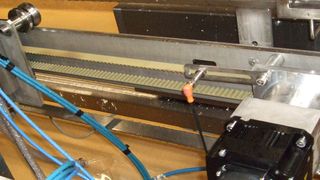 Der Servomotor treibt über einen Zahnriemen den Verfahrwagen an. Ein induktiver Sensor registriert den Abstand der Nocken auf dem Laufband, worüber die SPS die Geschwindigkeit des Verfahrwagens errechnet. (Bild: Mitsubishi Electric)