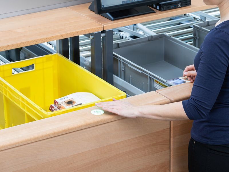 Die Waren werden bei der Kommissionierung mit der „Advanced-Pick-Station one-level“ von SSI Schäfer in Boxen auf ergonomischer Höhe abgelegt. Durch einfach zu bedienende Taster wird der Kommissioniervorgang bestätigt. (SSI Schäfer)