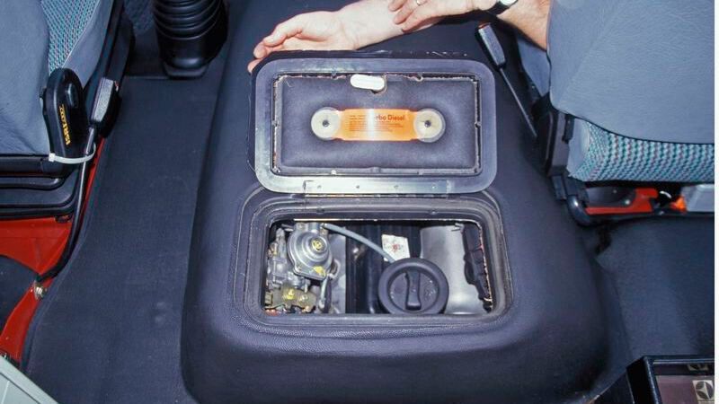 Die ab 1983 etwas schräger eingebauten Motoren erlaubten einen flacheren und weiter nach hinten gerückten Motorkasten. Ebenso entfiel der 2,0-Liter-Vierzylinder-Reihen-Ottomotor (stehend, hohe Motorabdeckung aus Blech) und es wurde ein Sechszylinderereihenbenzinmotor (schräg nach rechts geneigt, flache Motorabdeckung aus Kunststoff) mit 2,4 Liter Hubraum und Vergaser mit 66 kW (90 PS) verbaut. Im Zuge der Katalysatoreinführung wurde eine Digifant-Saugrohreinspritzung auf den Motor angepasst, mit der der 2,4-Liter-Otto-Motor nun 69 kW (94 PS) leistete. Beide Sechszylindermotoren sind konstruktiv um zwei Zylinder verlängerte Versionen des Volkswagen 1,6-Liter-Vierzylinder-Motors (ein Ableger des EA 827), es wurde allerdings wie bei den späteren Versionen des EA 827 der Wasserpumpenantrieb per Zahnriemen „vorweggenommen“.  (Bild: VWN)