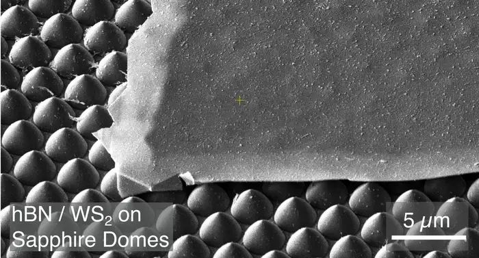 2D-Materialien: Ein Fall für Frischhaltefolie   Die modernen Materialwissenschaften arbeiten mit immer dünneren Schichten – mittlerweile bis zur Dicke einzelner Atome. Solche 2D-Materialien zeigen aufgrund der Quantenmechanik bemerkenswerte Eigenschaften, doch sie neigen auch zu Beschädigungen.  Die traditionelle Herstellungsmethode der letzten 22 Jahre – mit gewöhnlichem Klebeband – erzeugt winzige Risse und Bruchstücke von 2D-Materialien. Ein 2018 entwickeltes Verfahren mit Goldfolien ermöglichte zwar größere Schichten, scheiterte aber bei strukturierten Oberflächen mit Mustern oder Beschichtungen. Jetzt hat ein Amsterdamer Forschungsteam eine überraschend einfache Lösung gefunden: gewöhnliche Frischhaltefolie aus der Küche. Sie habe laut Forschern der Universität Amsterdam genau die richtigen Eigenschaften, um diese empfindlichen Materialien sanft und effektiv zu handhaben. Die Rasterlektronenmikroskop-Aufnahme oben zeigt ein 2D-Material-Flöckchen auf einer spitzen Oberfläche.       Hier geht‘s zur Originalmeldung Wissenschaftsbild des Tages vom 13.8.2026  (Bild: UvA IoP)