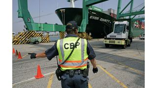 Ein CBP-Angestellter (Customs and Border Protection) leitet eine Zugmaschine mit einem Seehafencontainer in den Inspektionsbereich eines Hafens. (Amber Road)