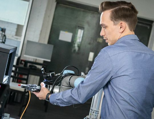 (Der Roboterarm wird von einem Mitarbeiter am Gelenk gesteuert und für eine Anwendung trainiert. Bild: Micropsi Industries)