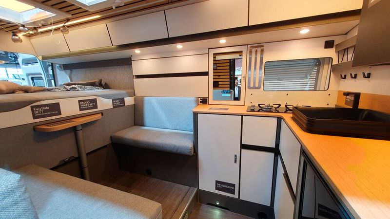 Der Innenraum ist von der Fahrerkabine getrennt. Ein Bad sucht man vergeblich, die faltbare Dusche verbirgt sich genauso wie die Chemietoilette verstaut in einem Fach. Dafür gibt es eine große L-förmige Küche, einen ausziehbaren Tisch und ein Heckbett, das sich zu einer gut zwei Meter breiten Liegewiese umwandeln lässt.  (Bild: Mauritz – VCG)