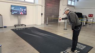 Mixed-Reality-Training bei Audi: Der Bildschirm im Hintergrund zeigt, was der Nutzer in der Brille sieht – gerade platziert er den Anschlussstutzen des Kühlmittel-Spülgerätes. Auf der schwarzen Fläche ist – nur für ihn sichtbar – das virtuelle Auto platziert. (Bild: Alina Seysen)