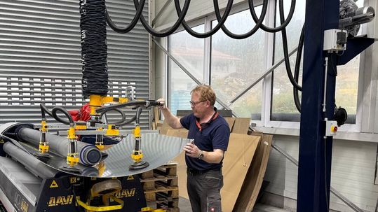 Mit dem Vakuum-Schlauchheber „heavyLIFT“ von Timmer entnimmt ein Mitarbeiter von Lo-Cat Systems das gewölbte Aluminiumblech präzise und schonend aus der Rundwalze.(Bild:  Lo-Cat Systems)