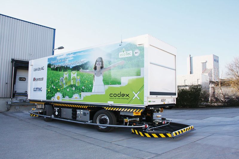 Während das Fahrzeug sich an die unterschiedlich hohen Rampen der einzelnen Hallen andockt und mittels eines Kettenförderantriebs vollautomatisch 14 Paletten einzieht, fährt ein Ladefinger aus und versorgt den Akku während der Beladung mit Ladestrom.  (Kamag)