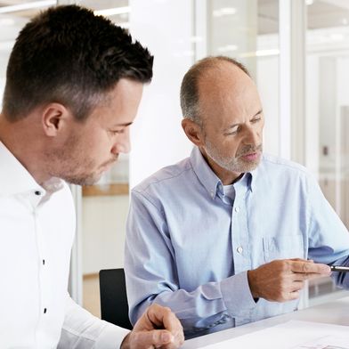 Im Austausch über Maschinensicherheit: Zwei Experten prüfen einen Sicherheitssensor und technische Planungsunterlagen – ein wichtiger Schritt für sichere Maschinen und die Umsetzung neuer Anforderungen. (Bild: Leuze Electronic GmbH + Co. KG)