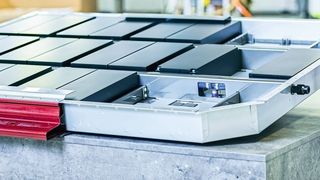 Batteriekasten mit einem Ausschnitt des Crash-Rahmens (links unten in rot) und einem angedeuteten Deckel. Das Sichtfenster im Längsträger ermöglicht einen Blick auf die Steigleitung, die das Kühlmediums zuführt. (Benteler)