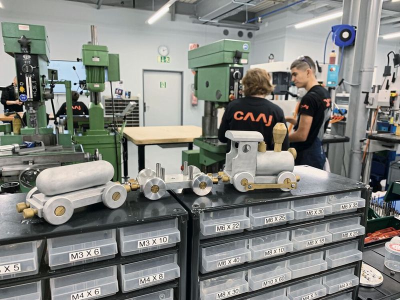 Réalisation faite par les apprentis en premier plan, en second plan, les apprentis se forment sur des machines à cames. (Source : CAAJ Moutier)