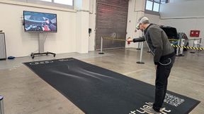 Mixed-Reality-Training bei Audi: Der Bildschirm im Hintergrund zeigt, was der Nutzer in der Brille sieht – gerade platziert er den Anschlussstutzen des Kühlmittel-Spülgerätes. Auf der schwarzen Fläche ist – nur für ihn sichtbar – das virtuelle Auto platziert. (Bild: Alina Seysen)